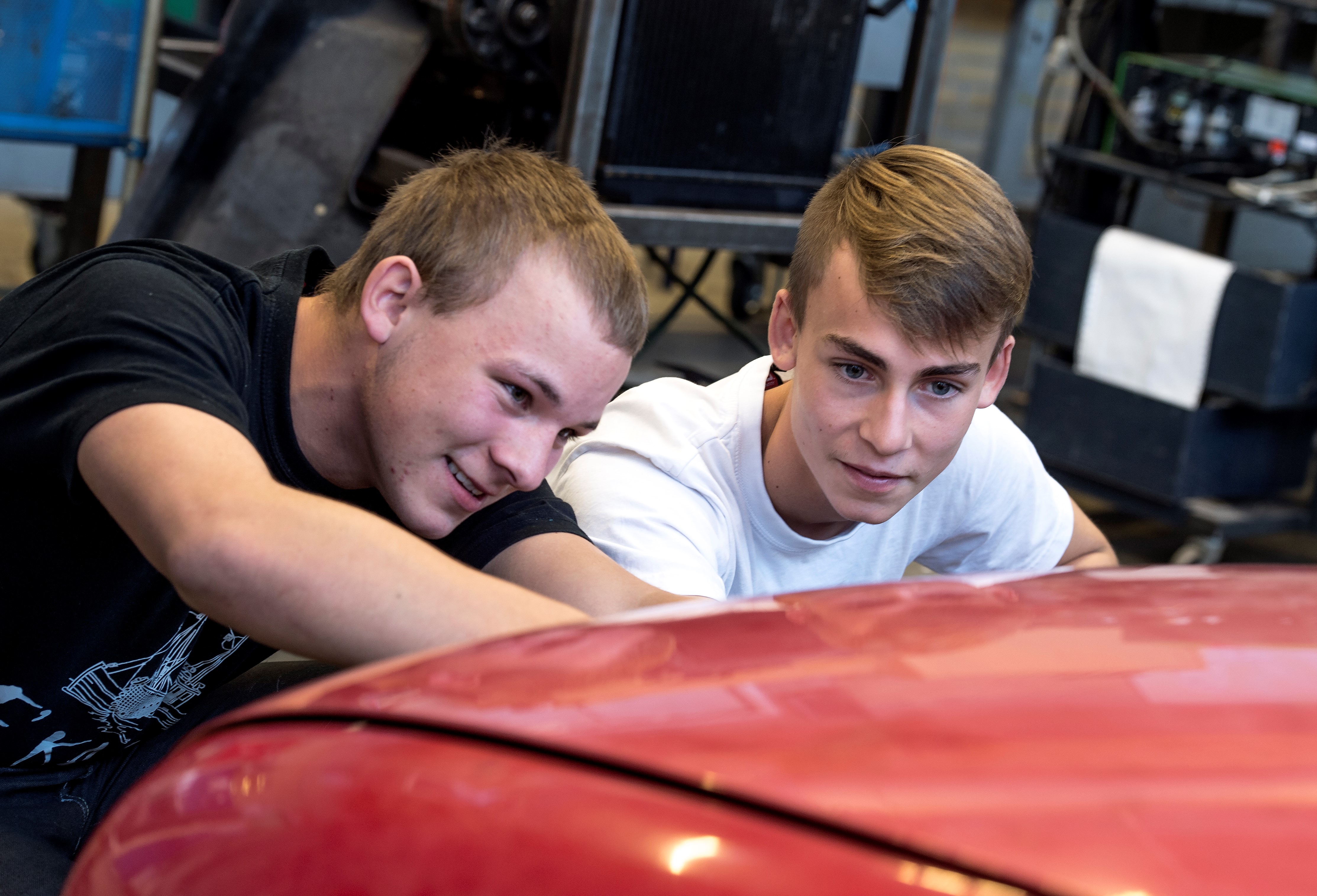 To unge elever inspicerer fokuseret lakken på køleren på en personbil.